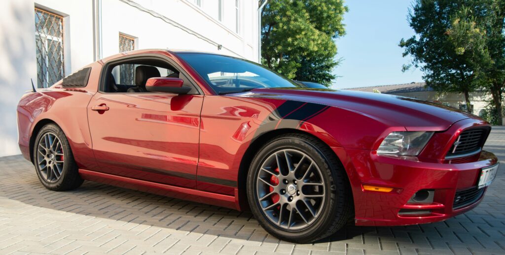 A striking red Mustang parked in a sunlit driveway, showcasing its sporty design.