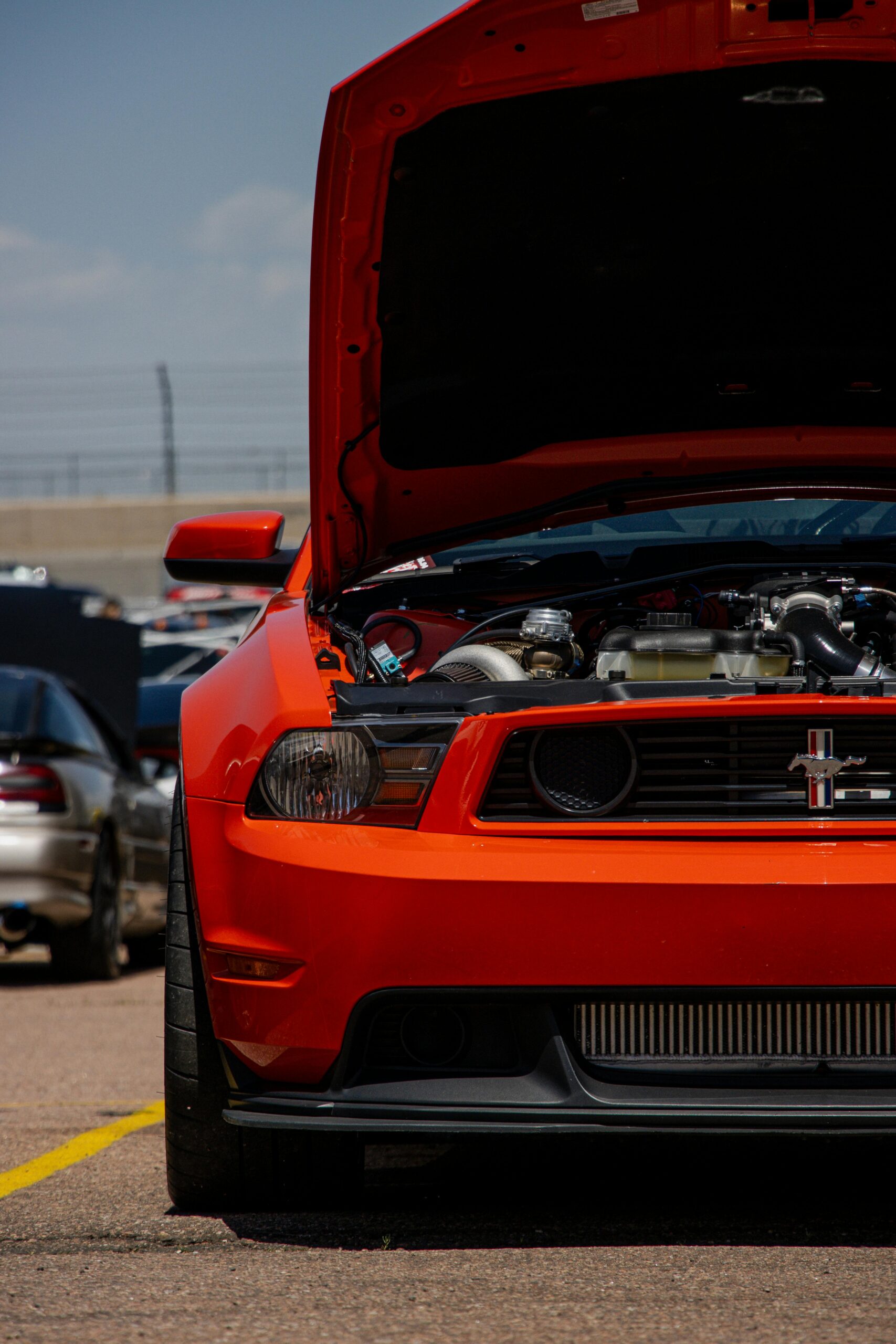 Close-up of a striking red Ford Mustang with its hood open at an outdoor car show.