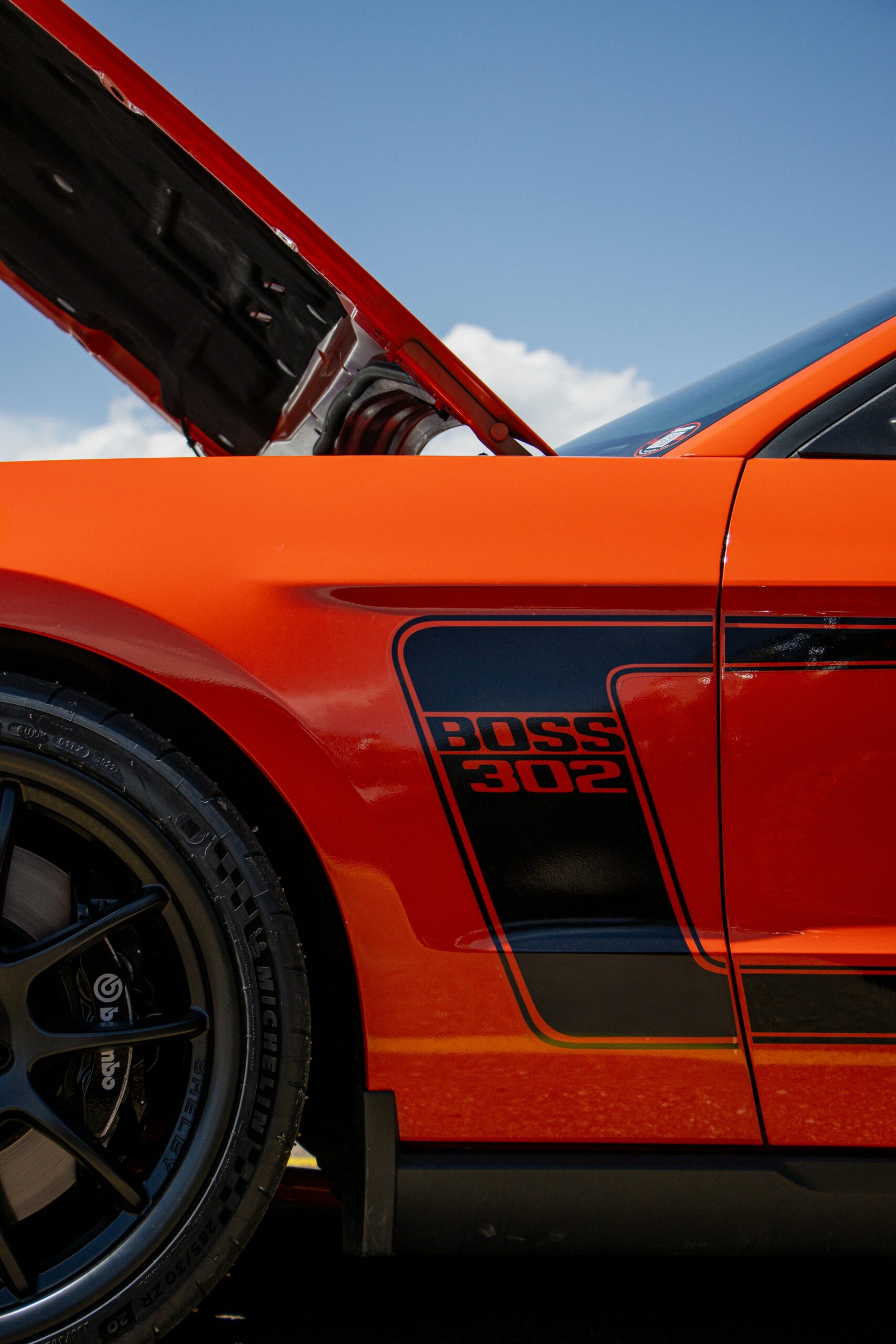 Detailed side view of a vibrant red Boss 302 Ford Mustang under a clear sky.